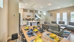 A modern kitchen with white cabinets, a central island, and a dining area with a wooden table set for four. - NEW! Stylish Houston Townhome ~ 3 Mi to Downtown! (Houston)