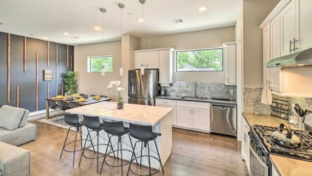 A modern kitchen with a central island, bar stools, stainless steel appliances, and a view of greenery outside. - NEW! Stylish Houston Townhome ~ 3 Mi to Downtown! (Houston)
