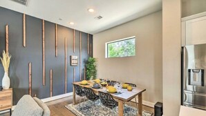 A modern dining area with a wooden table set for six, a dark accent wall, and a kitchen with a stainless steel refrigerator. - NEW! Stylish Houston Townhome ~ 3 Mi to Downtown! (Houston)