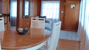 Une pièce aux murs lambrissés, avec une table de salle à manger ronde, des chaises blanches, un ventilateur de plafond et une porte dotée d’une petite fenêtre.