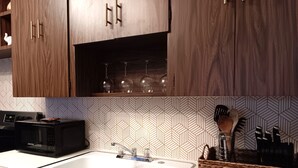 Une cuisine avec des meubles en bois, un évier blanc, un four à micro-ondes et un crédence décorée.