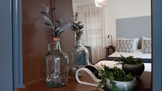 Une chambre à coucher comprenant un lit, une table de chevet et une petite table de nuit ornée de bouteilles en verre décoratives et d’une plante en pot.