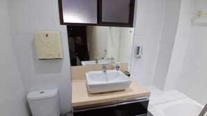 A compact bathroom with a white toilet, a sink with a mirror above, a black oven, and a white bathtub. - Nadi Airport Transit Hotel (Nadi)