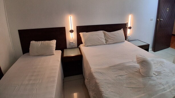 A hotel room with two single beds, each with a nightstand and a wall-mounted lamp. - Nadi Airport Transit Hotel (Nadi)