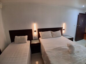 A hotel room with two single beds, each with a nightstand and a wall-mounted lamp.