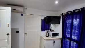 A small room with a white door, a white cabinet, a microwave, a television, and a blue curtain. - Nadi Airport Transit Hotel (Nadi)
