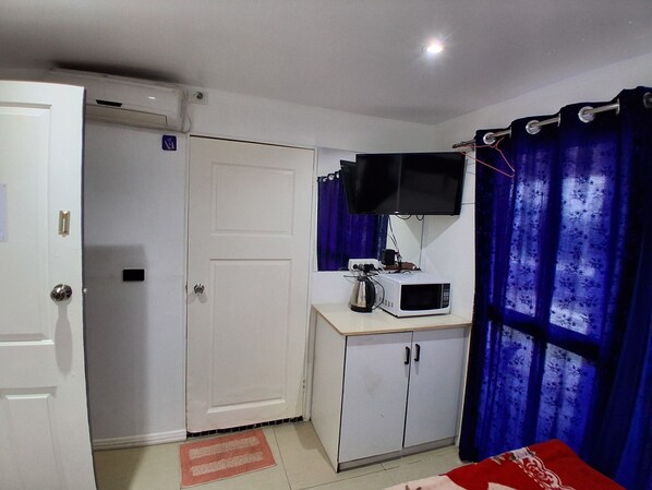 A small room with a white door, a white cabinet, a microwave, a television, and a blue curtain.