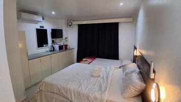 A hotel room with a bed, bedside table, and a small kitchenette area.