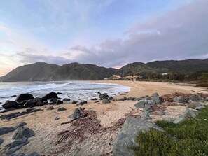 A beach with rocky foreground, waves, and a mountainous backdrop.