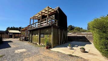 A rustic wooden building with a balcony, gravel driveway, and potted plants.