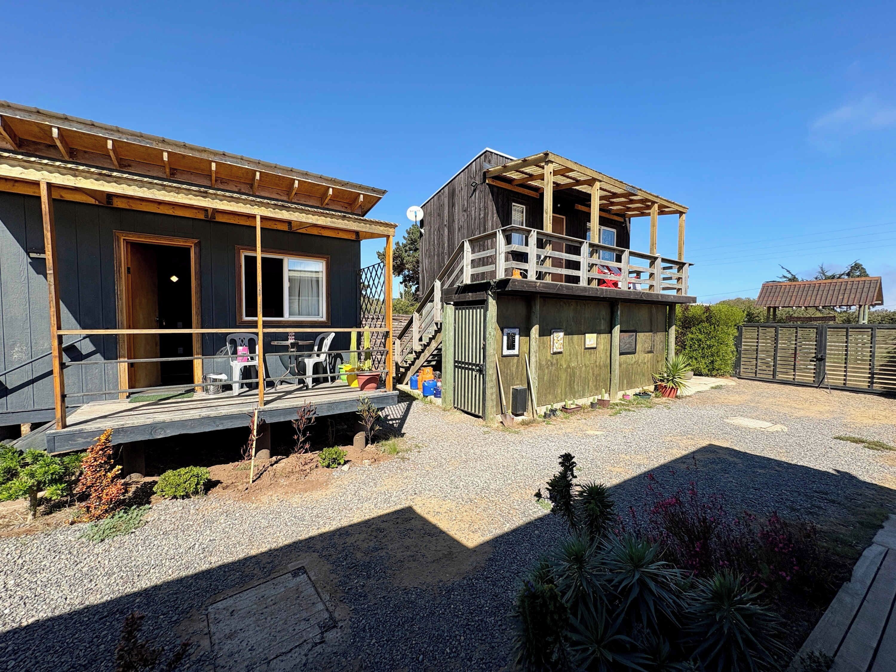 A wooden cabin with a balcony, a covered porch, and a gravel driveway.