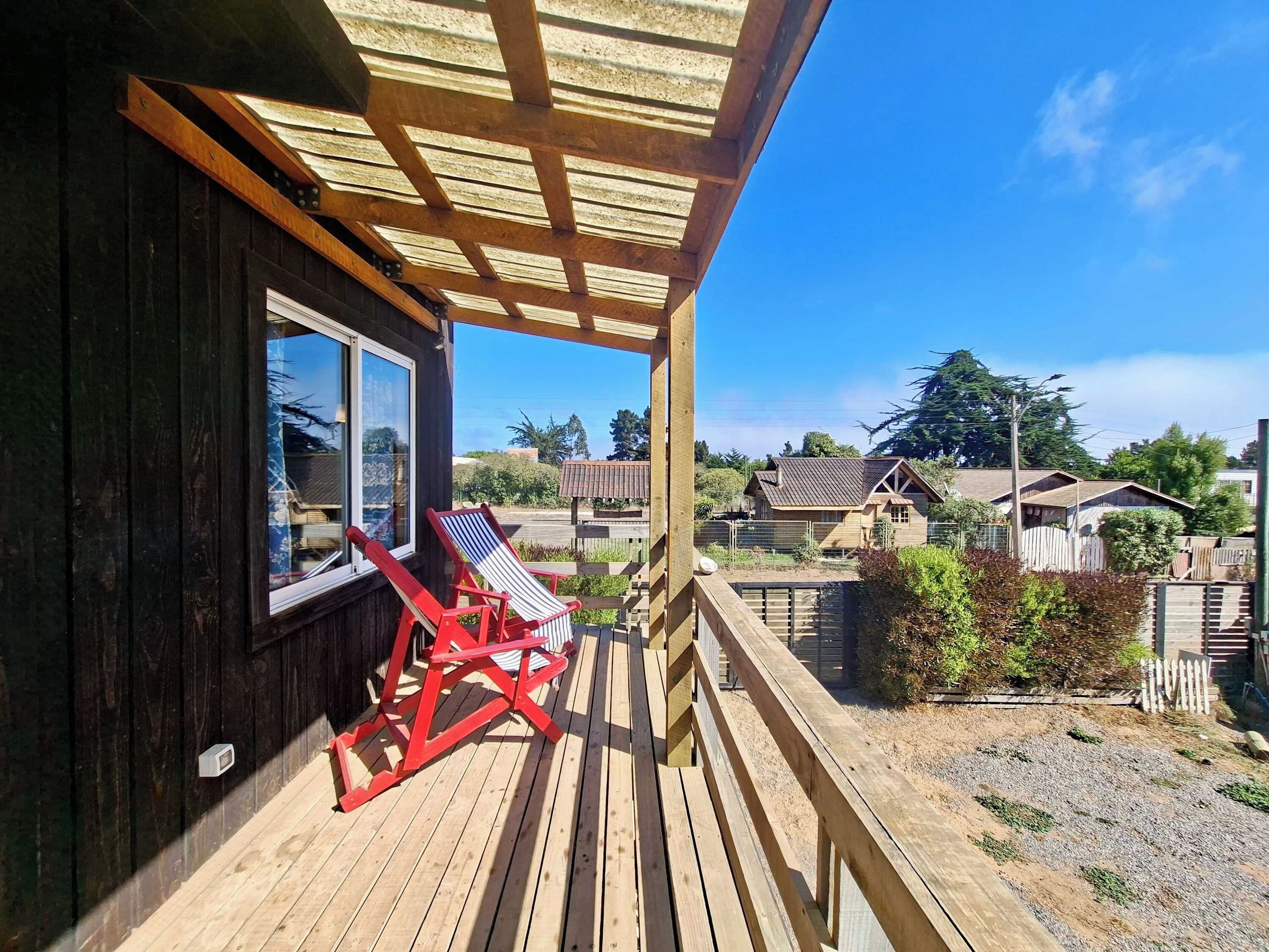 A wooden deck with a covered area, a window, and a red chair.