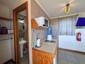 Uma cozinha compacta equipada com micro-ondas, dispenser de água e uma pia pequena.