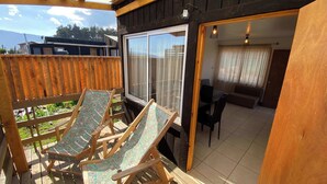 A wooden deck with two lounge chairs, a sliding glass door leading to a living area, and a view of the outdoors. - Wheelchair-Friendly Cabin - BBQ, Parking & Wifi (Quintay)