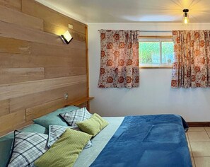 Ein Schlafzimmer mit einem Bett, Kissen, einem Holz-Kopfteil, einem Fenster mit Vorhängen und einer Wandleuchte.