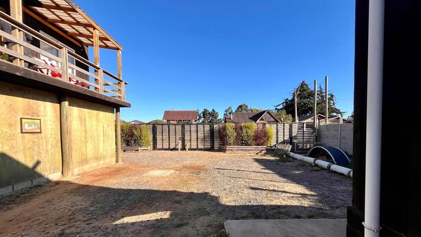 A gravel driveway leading to a fenced area with a wooden structure on the left and a metal gate in the distance. - Wheelchair-Friendly Cabin - BBQ, Parking & Wifi (Quintay)