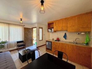 Una cocina compacta con armarios de madera, una mesa de comedor, sillas, microondas y tetera.