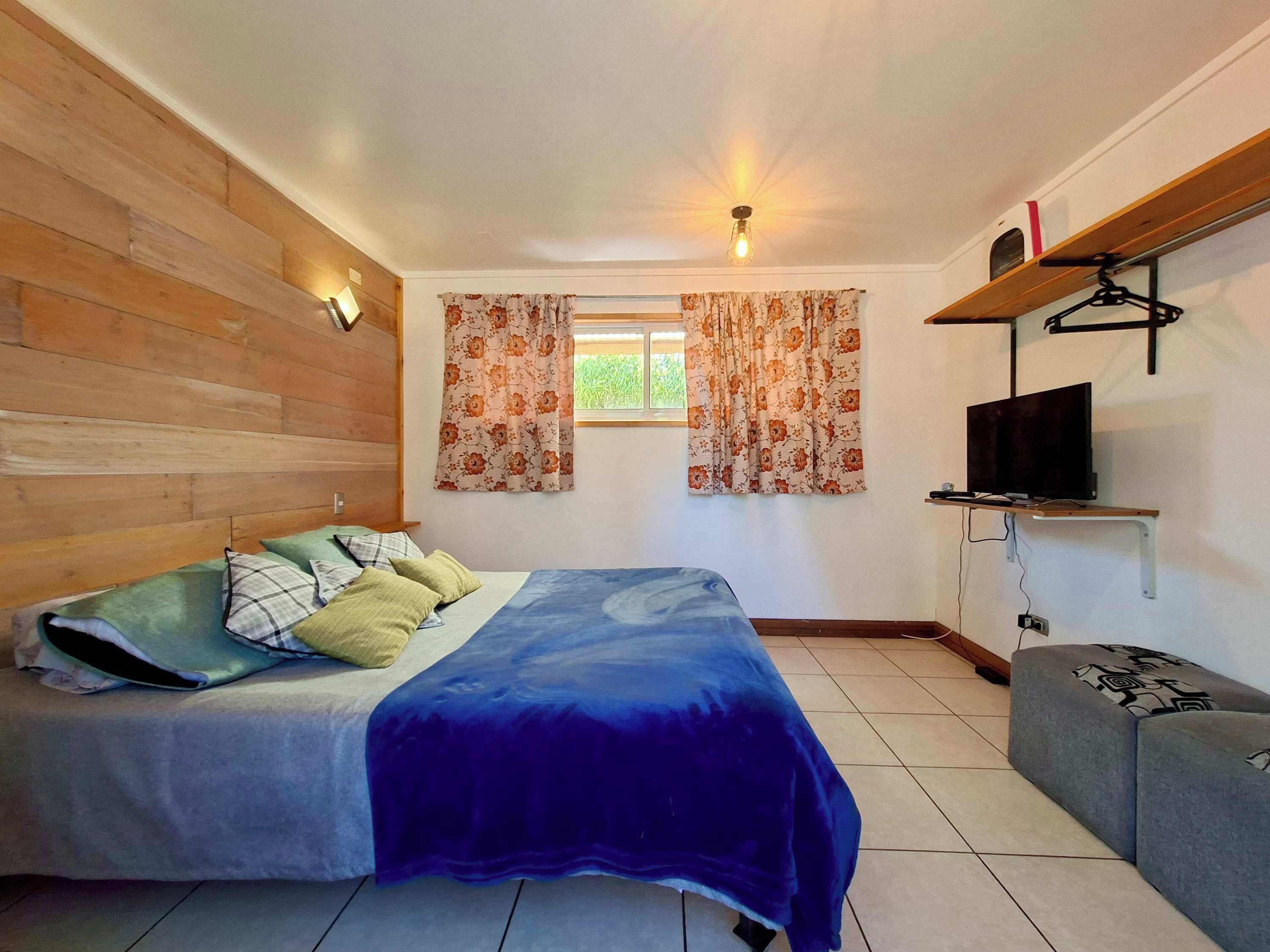 A bedroom with a bed, a TV mounted on a shelf, and a window with curtains.