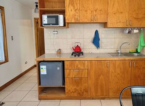 Eine kompakte Küche mit Holzausstattung, einer Mikrowelle, einem Wasserkocher, einer Spüle und einem kleinen Kühlschrank.