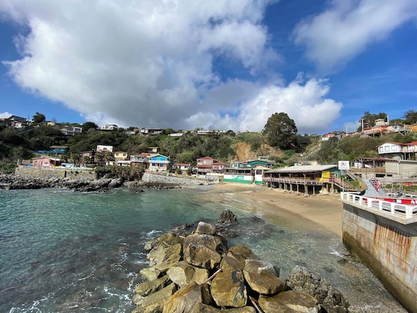 Une ville côtière avec des maisons construites sur une colline, une plage et une jetée où sont amarrés des bateaux.