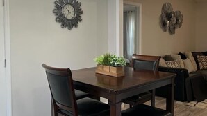 Un espace repas comprenant une table en bois, des chaises foncées, un lustre, une horloge murale et un élément décoratif mural.