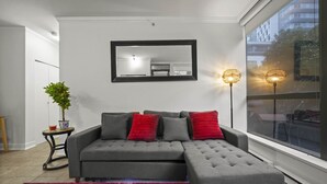 En moderne stue med en grå modulsofa, røde puder, et stort spejl og en gulvlampe.