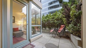 En moderne bygning med en glasindgang, en terrasse med stol og bord, og udsigt til et skovområde.