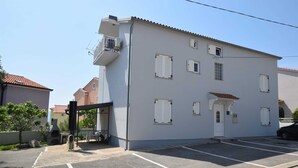 A two-story building with a white facade, multiple windows with shutters, and a small porch area. - Apartment Fejer 1 with balcony (Njivice)