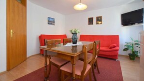 A dining area with a wooden table and chairs, a red sofa, a vase with flowers, and a television on the wall. - Apartment Fejer 1 with balcony (Njivice)
