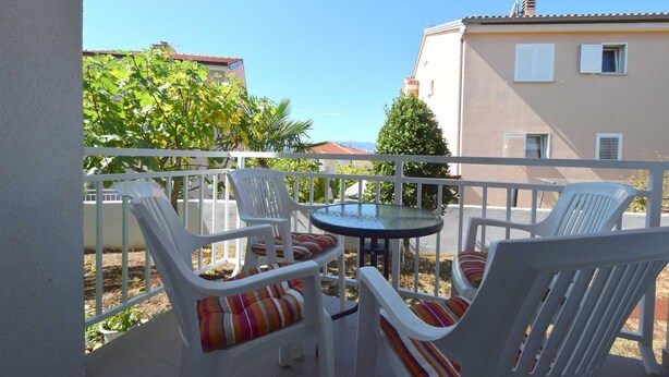 A balcony with white chairs and a small round table, overlooking a residential area with trees and buildings. - Apartment Fejer 1 with balcony (Njivice)