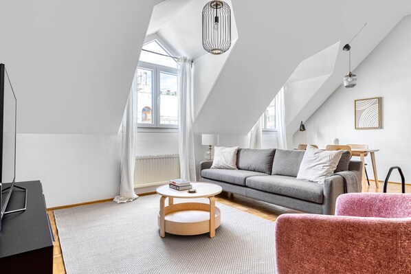 Un loft moderno con techo alto, un sofá gris, una silla rosa y una mesa de centro redonda de madera.