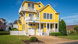 A two-story yellow house with a white porch, a garage, and a well-maintained lawn.