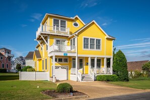 A two-story yellow house with a white porch, a garage, and a well-maintained lawn. - Just Coasting: Private pool, hot tub, community pools, Currituck Club amenities (Corolla)