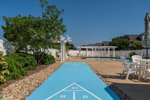A poolside area with a blue shuffleboard court, white outdoor furniture, and a white fence. - Just Coasting: Private pool, hot tub, community pools, Currituck Club amenities (Corolla)