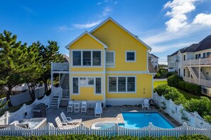 A two-story yellow house with a swimming pool, white deck chairs, and a fenced backyard.