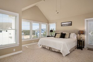 A bedroom with a large bed, multiple windows, and a view of a house. - Just Coasting: Private pool, hot tub, community pools, Currituck Club amenities (Corolla)