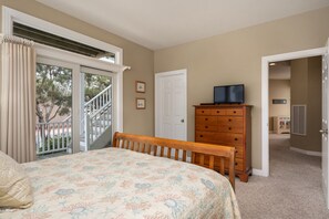 A bedroom with a bed, a dresser, a television, and a door leading to another room.