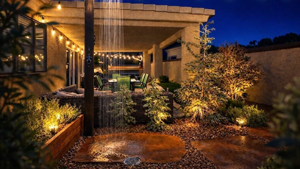 Un patio con fuente de agua, mobiliario exterior e iluminación con luces colgantes.