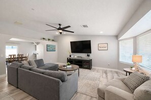 Ein modernes Wohnzimmer mit einem grauen Ecksofa, einem beige Armlehnstuhl, einem Couchtisch und einem an der Wand befestigten Flachbildfernseher.