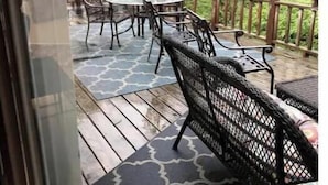 Eine Terrasse im Freien mit Holzdeck, Metallstühlen, einem runden Tisch und einem Grill.