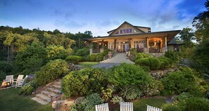 A large, two-story house with a covered porch, surrounded by lush greenery and a stone pathway leading to the entrance.