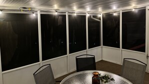 A covered patio area with a table and chairs, large windows, and string lights. - Countryside Home, Dog Friendly, Large Yard, Near Several Lakes (Alexandria)