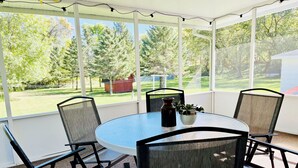 A covered patio with a round table and four chairs, a vase with plants, and a view of a green landscape. - Countryside Home, Dog Friendly, Large Yard, Near Several Lakes (Alexandria)