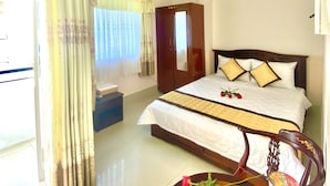 A hotel room with a bed, a bedside table with a vase of flowers, a mirror, and a wardrobe. - Nama Hotel (Can Tho)