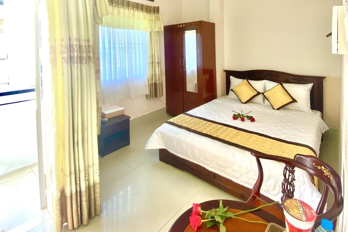 A hotel room with a bed, a bedside table with a vase of flowers, a mirror, and a wardrobe.