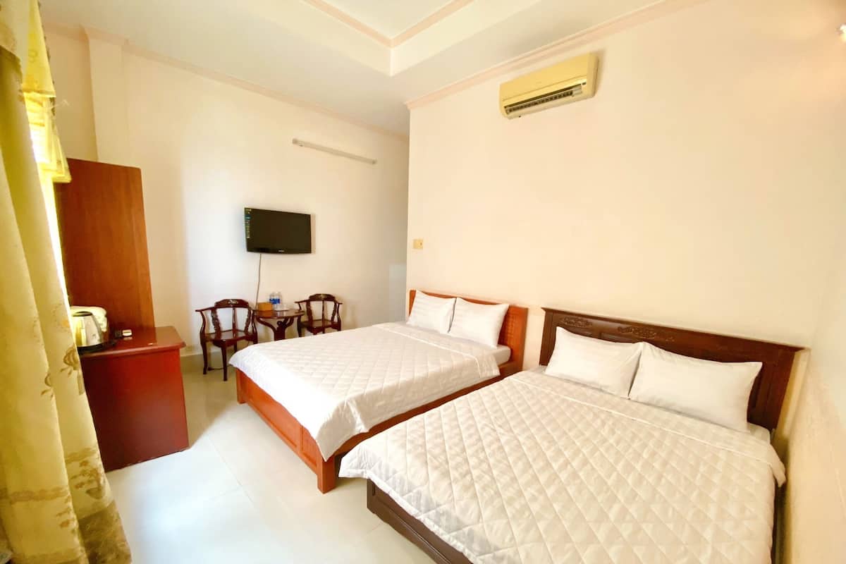 A hotel room with two beds, a desk, chairs, a television, and an air conditioning unit.