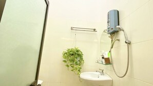 A small bathroom with a skylight, a sink, a handheld showerhead, and a potted plant. - Nama Hotel (Can Tho)