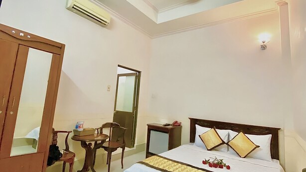 A hotel room with a bed, a desk, a chair, a wardrobe, and a ceiling light. - Nama Hotel (Can Tho)