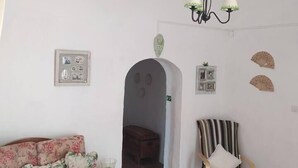 Ein Wohnzimmer mit einem floralen Sofa, einem Holzstuhl, einem Tisch mit gemustertem Tischläufer und einer Chandelüster.