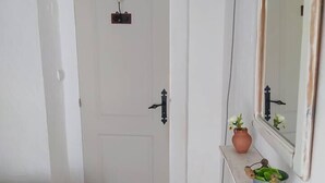 Ein schmaler Flur mit einer weißen Tür, einem kleinen Regal mit einer Topfpflanze und einer Wand-Klimaanlage.